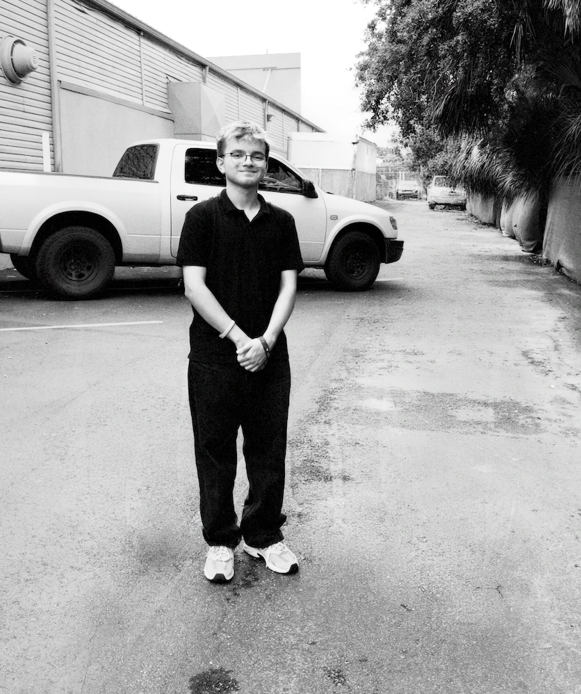 Matheus Charone standing in front of a white pickup truck, black and white